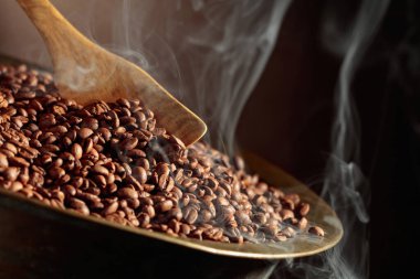 Orta pişmiş kahve çekirdekleri kızartma tavasında dumanlıdır. Boşluğu kopyala.