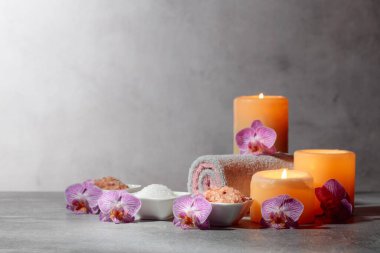 Deniz tuzu, havlular, orkide çiçekleri ve gri arka planda yanan mumlar. Kopyalama alanı ile kaplıca kavramı.