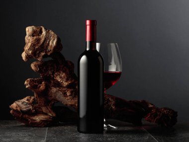 Siyah taş bir masanın üzerinde şişe ve bir bardak kırmızı şarap. Arka planda eski yıpranmış bir pürüz var. Kopyalama alanı ile ön görünüm.