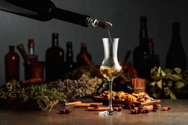 Sarı bitkisel likör ya da merhem eski bir şişeden bardağa dökülür. Kurutulmuş otlar, çiçekler, baharatlar ve eski mutfak aletleri. Bitkisel ilaç kavramı.