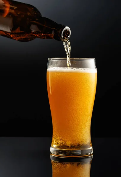 ボトルからグラスにビールを注ぐ 黒の反射的背景のビールのガラス — ストック写真