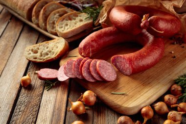 Smoked sausage with rosemary, onion and pepper. Sausage with bread and spices on a old wooden table. clipart