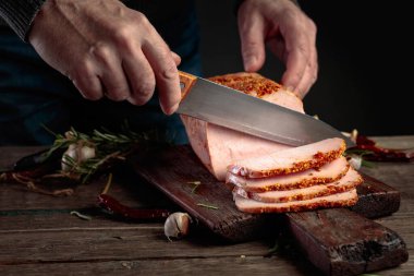 Eski ahşap bir masada baharatlı jambon kesen bir erkek kasap elleri. Noel yemeği.
