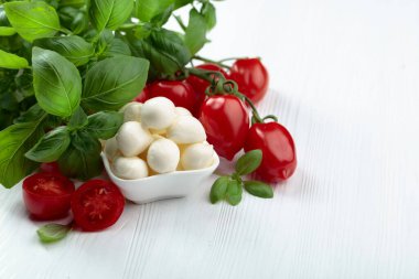 Beyaz ahşap bir masada fesleğenli ve domatesli Mozzarella peyniri. Geleneksel İtalyan atıştırması.