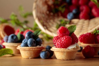 Küçük tartlar taze ahududu ve böğürtlenlerle süslenmiş ahşap bir masada nane ile.