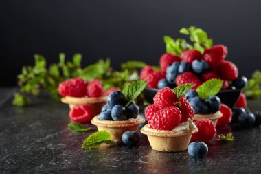 Siyah arka planda naneli taze ahududu ve yaban mersinli küçük tartlar..