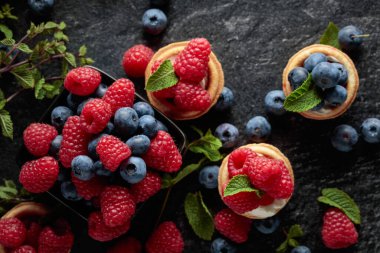 Siyah arka planda naneli taze ahududu ve yaban mersinli küçük tartlar. Üst görünüm.