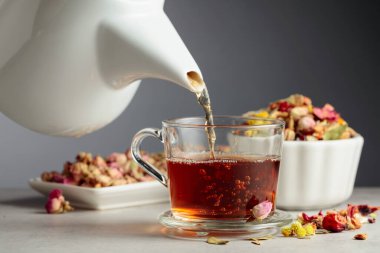 Bitki çayı bardağa dökülür. Kurumuş otlar ve çiçekler taş masaya saçılmış..