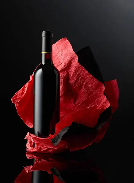 Bottle of red wine on a crumpled paper. Black reflective background.
