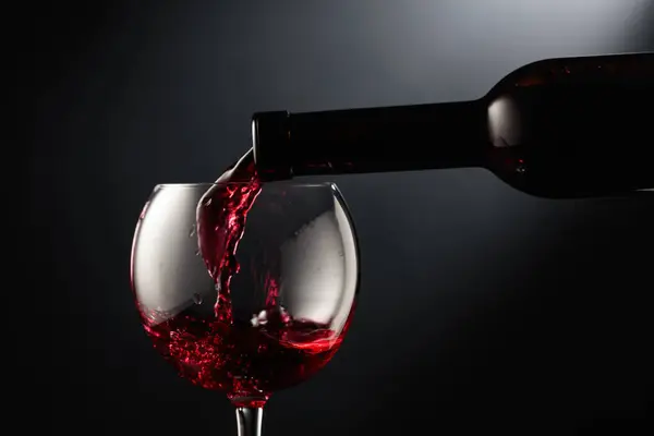 Pouring red wine into a wine glass on a black background.