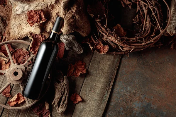 Bottle of red wine on a vintage rustic background with old wood and dried-up vine leaves. Concept of old wine. Copy space.