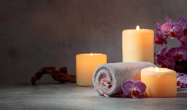 Towels, orchid flowers, and burning candles on a grey background. Spa concept with copy space.