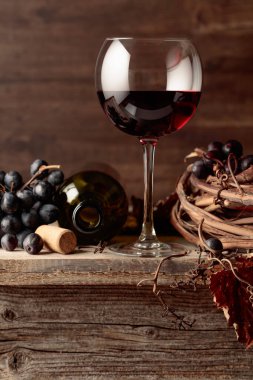 Eski ahşap bir masada üzümlü bir bardak ve bir şişe kırmızı şarap..