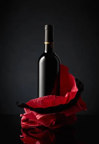 在皱皱巴巴的纸上的一壶红葡萄酒 黑色反光背景 — 图库照片