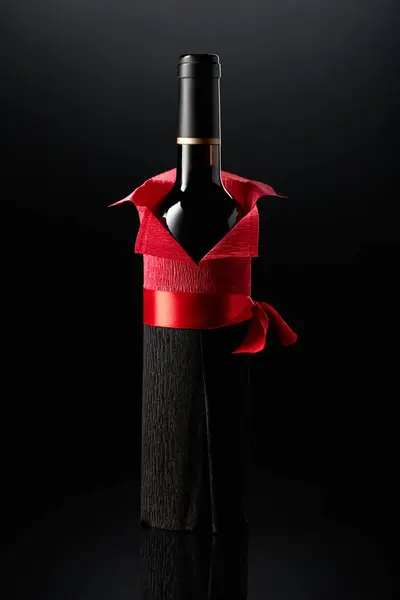 Bottle of red wine wrapped in crepe paper on a black background. The bottle looks like a man in a red shirt.