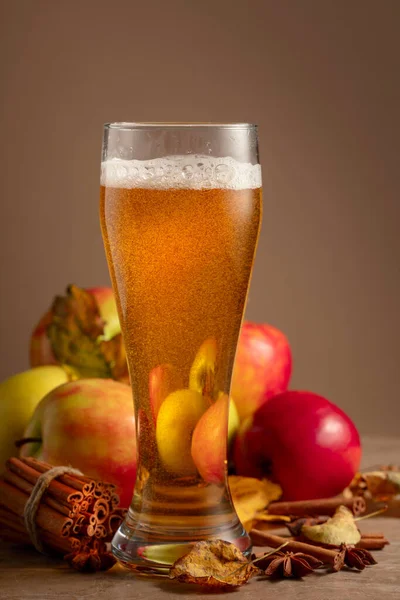 Apple cider in high glass. Fresh carbonated drink with apples, cinnamon, and anise on a beige background.