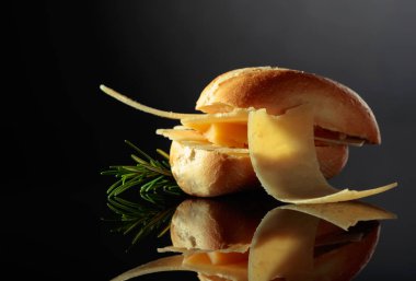 Sandwich with Parmesan cheese and rosemary on a black reflective background.