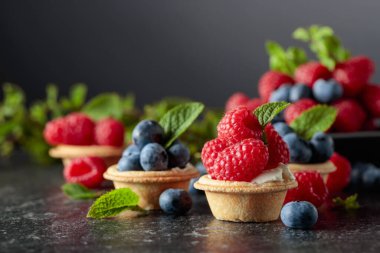 Siyah arka planda naneli taze ahududu ve yaban mersinli küçük tartlar..