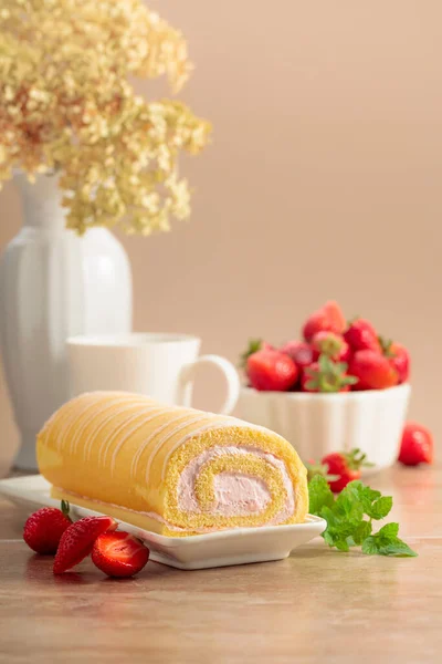 Homemade strawberry biscuit cake roll with cream cheese, whipped cream, and fresh berries. Delicious biscuit cake with strawberries on a beige background.