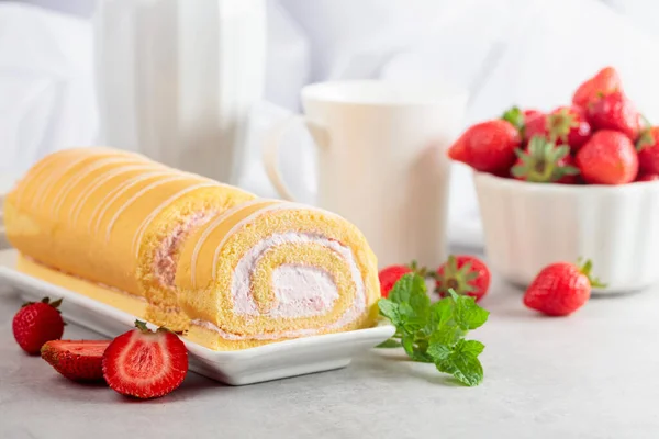 Homemade strawberry biscuit cake roll with cream cheese, whipped cream, and fresh berries. Delicious biscuit cake with strawberries on a white table.