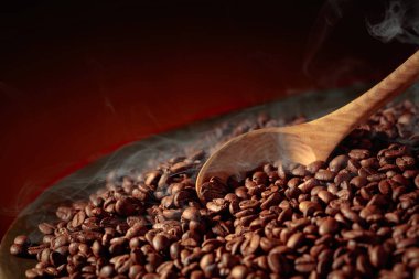 Orta pişmiş kahve çekirdekleri kızartma tavasında dumanlıdır. Boşluğu kopyala.