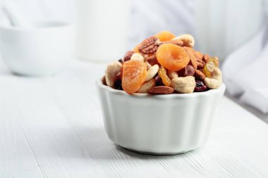 Beyaz ahşap bir masada kurumuş meyve ve çeşitli fındıklar..