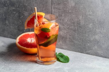Buzlu çay, naneli ve greyfurtlu. Gri arka planda malzemeleri olan soğuk, ferahlatıcı bir içecek. Boşluğu kopyala.