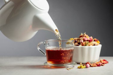 Bitki çayı bardağa dökülür. Kurumuş otlar ve çiçekler taş masaya saçılmış..