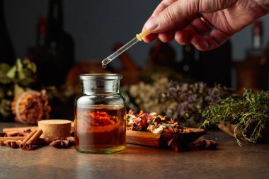 Temel bitkisel tentürü küçük bir cam şişeye atmak. Kurutulmuş otlar, çiçekler, baharatlar ve eski mutfak aletleri. Bitkisel ilaç kavramı.