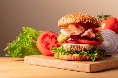 Tahta kesme tahtasında taze lezzetli bir burger. Domatesli burger, soğan, korunmuş salatalık, salata, peynir, sığır pirzolası ve pastırma. Boşluğu kopyala.