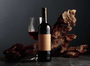 Boş etiketli bir şişe ve bir bardak kırmızı şarap. Arka planda eski yıpranmış bir pürüz var. Kopyalama alanı ile ön görünüm.