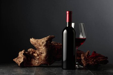 Siyah taş bir masanın üzerinde şişe ve bir bardak kırmızı şarap. Arka planda eski yıpranmış bir pürüz var. Kopyalama alanı ile ön görünüm.