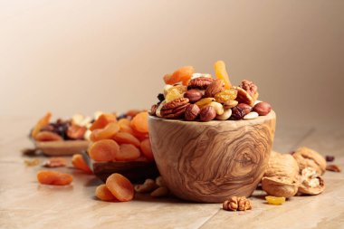 Dried fruits and nuts on a beige ceramic table. The mix of nuts, apricots, and raisins in a wooden bowl. Copy space.