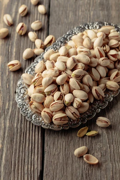 Salted pistachios in a dish on an old wooden table.