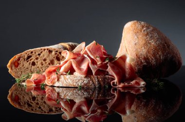 Siyah yansıtıcı arka planda ciabatta ve kekik ile Prosciutto.