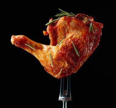 Grilled chicken leg sprinkled with rosemary on a black background. Chicken drumstick on a fork. clipart