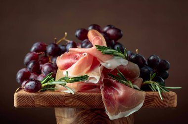 Ahşap bir masada üzümlü ve biberiyeli jambon..