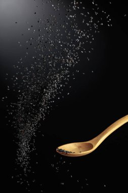 Tahta kaşıkla siyah susam taneleri dökülür. Karanlık bir arka planda siyah susam. Boşluğu kopyala.