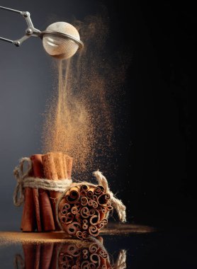 Cinnamon powder is poured out of the strainer. The ground cinnamon, cinnamon sticks, tied with jute rope on a black reflective background. Copy space.