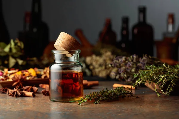 Essential herbal tincture in a small glass bottle. On a table dried herbs, flowers, spices, and old kitchen utensils. Alternative or complementary medicine treatment.
