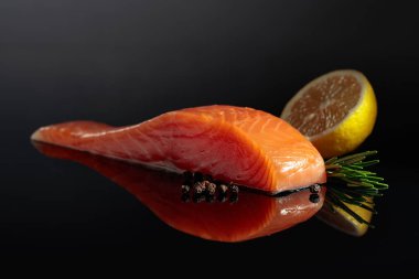 Smocked salmon piece with rosemary, lemon, and peppercorn on a black reflective background.