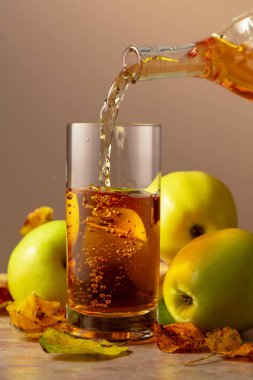 Elma şarabı şişeden bardağa dökülür. Seramik bir masada olgun elmalar ve kurumuş yapraklar..