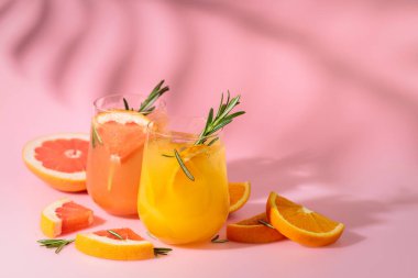 Greyfurt, portakal, biberiye ve buzlu yaz kokteylleri. İçkiler pembe arka planda, palmiye yaprağı gölgesinde. Boşluğu kopyala.