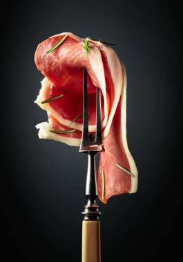 Sliced prosciutto with rosemary on a fork.