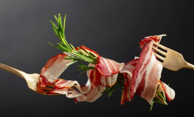 Siyah arka planda biberiyeli kurutulmuş domuz pastırması. Çatalda dilimlenmiş pastırma..