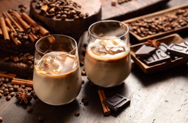 Eski ahşap arka planda buzlu bardakta İrlanda kreması ve kahve kokteyli. Kahve çekirdekleri, tarçın, anason ve çikolata parçaları masaya saçıldı.. 