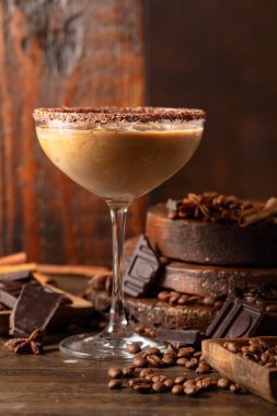 Eski ahşap arka planda buzlu bir bardakta İrlanda kreması ve kahve kokteyli. Kahve çekirdekleri, tarçın, anason ve çikolata parçaları masaya saçıldı.. 