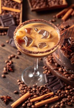 Eski ahşap arka planda buzlu bir bardakta İrlanda kreması ve kahve kokteyli. Kahve çekirdekleri, tarçın, anason ve çikolata parçaları masaya saçıldı.. 