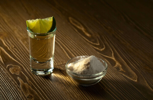 Tequila with salt and lime on old wooden table.