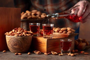 İtalyan likörü Amaretto. Eski bir masada badem fıstıklı. Likör şişeden bardağa dökülür..